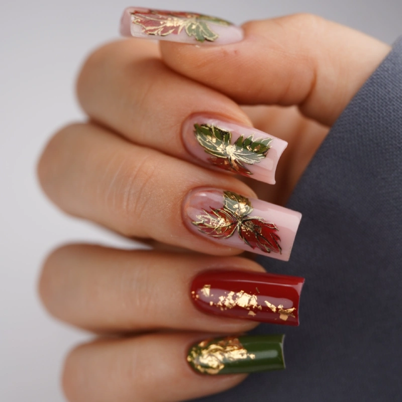 Red nails with gold leaves and green accents on a nude base