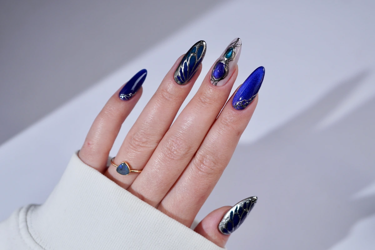 Sapphire nails with metallic details and gemstone-inspired effects on long almond-shaped nails