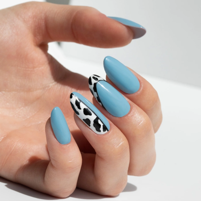 Ongles bleus avec motif cow print noir et blanc dans une manucure animal print