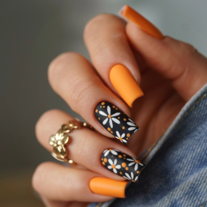 Orange and black pumpkin spice nails with white flowers.